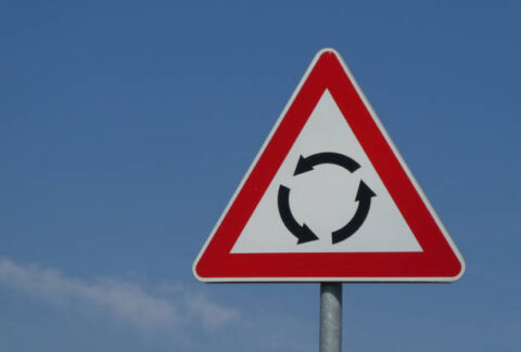 Circular Intersection - warning traffic road sign roundabout against blue sky